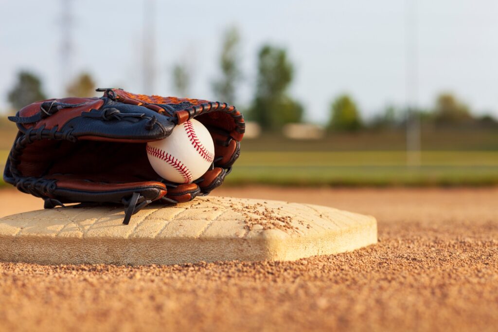 Selective focus of baseball in leather mitt on base of a baseball park infield on a sunny afternoon